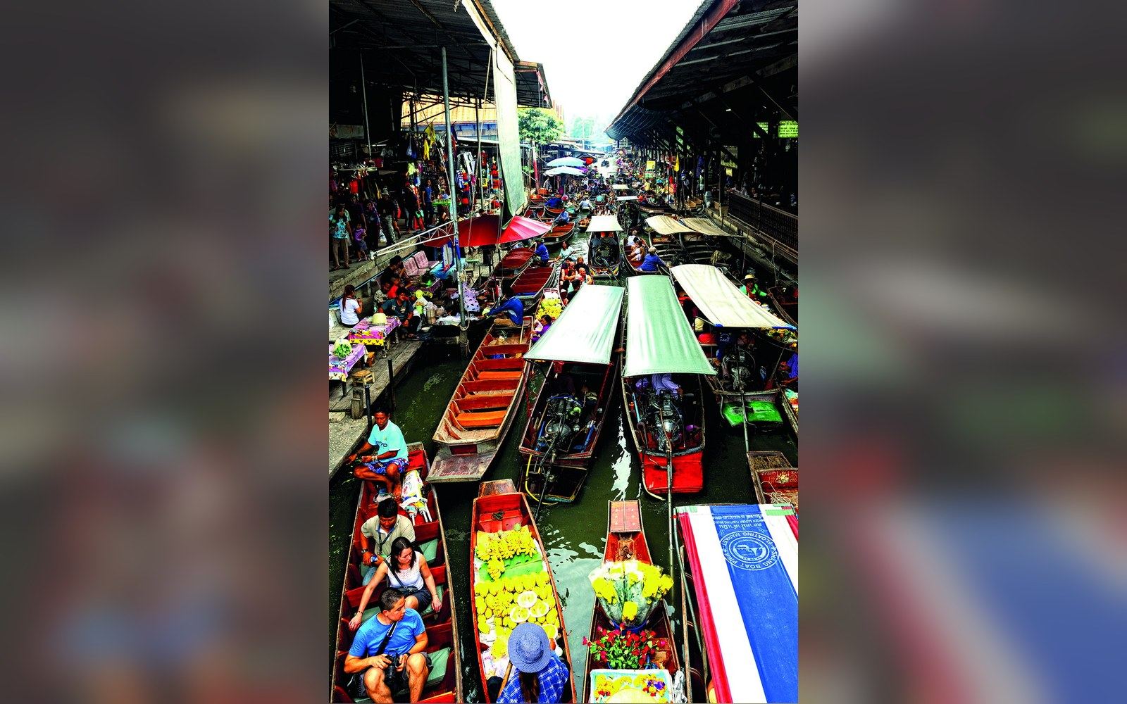 Long-tail wooden boats loaded with produce crowd a narrow canal at a floating market