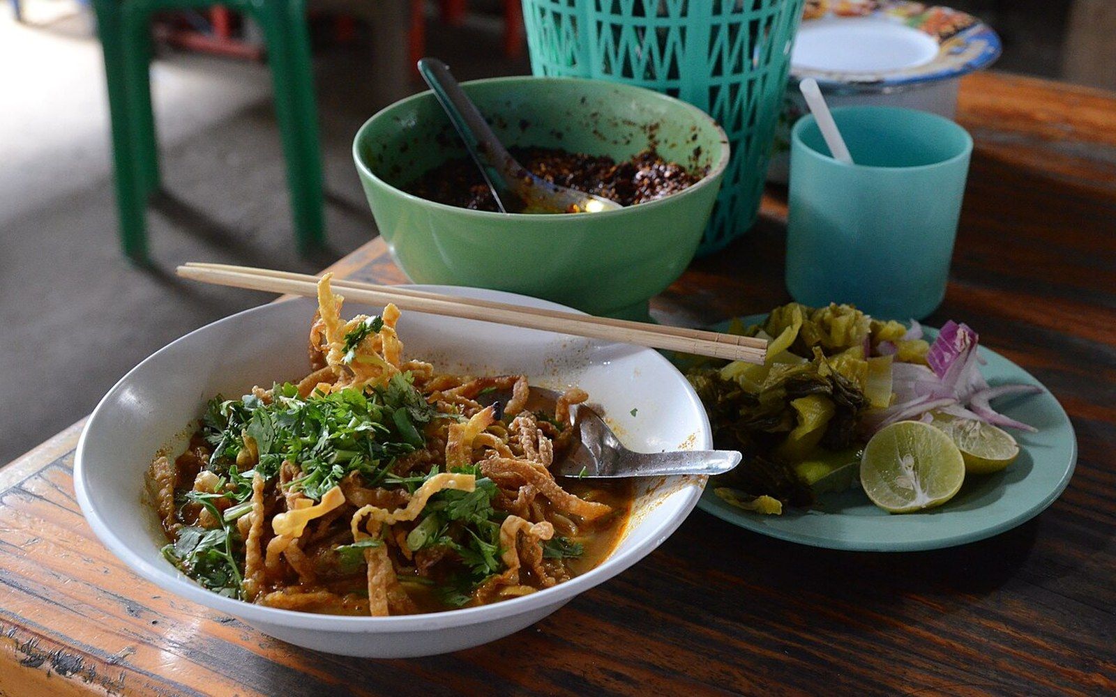 Bowl of khao soi noodle soup topped with crispy noodles, served with pickled greens and lime
